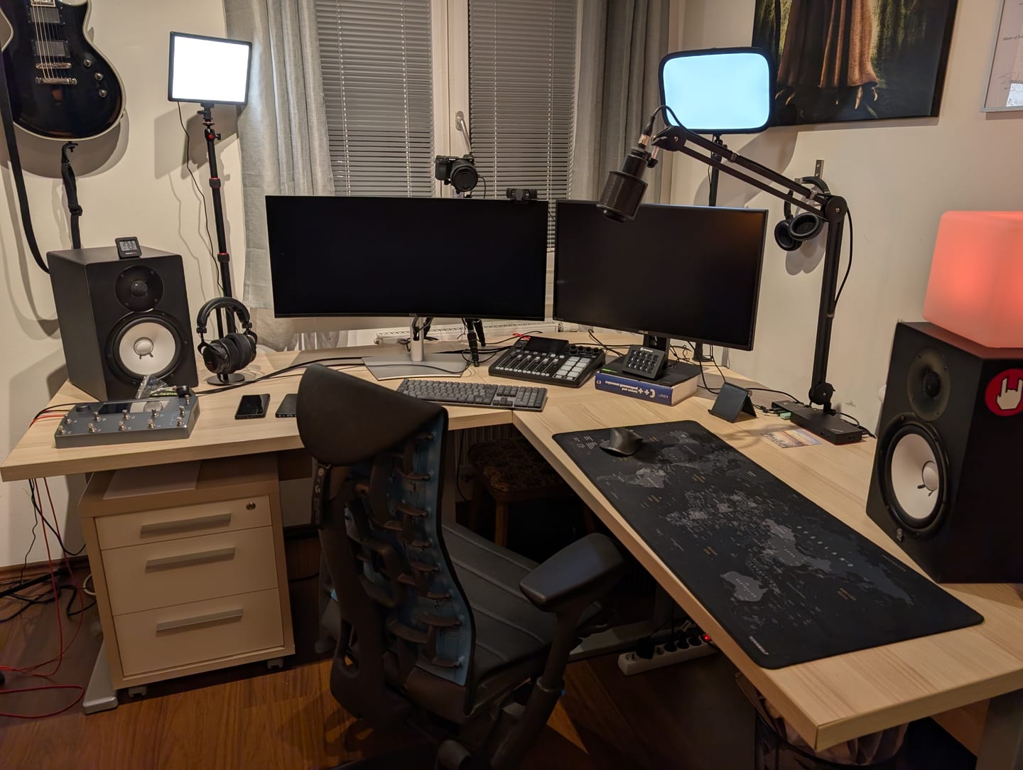 Der Schreibtisch mit zwei Monitoren, Mikrofon am Schwenkarm, Stream Deck, Studiomonitoren und einer Gitarre an der Wand